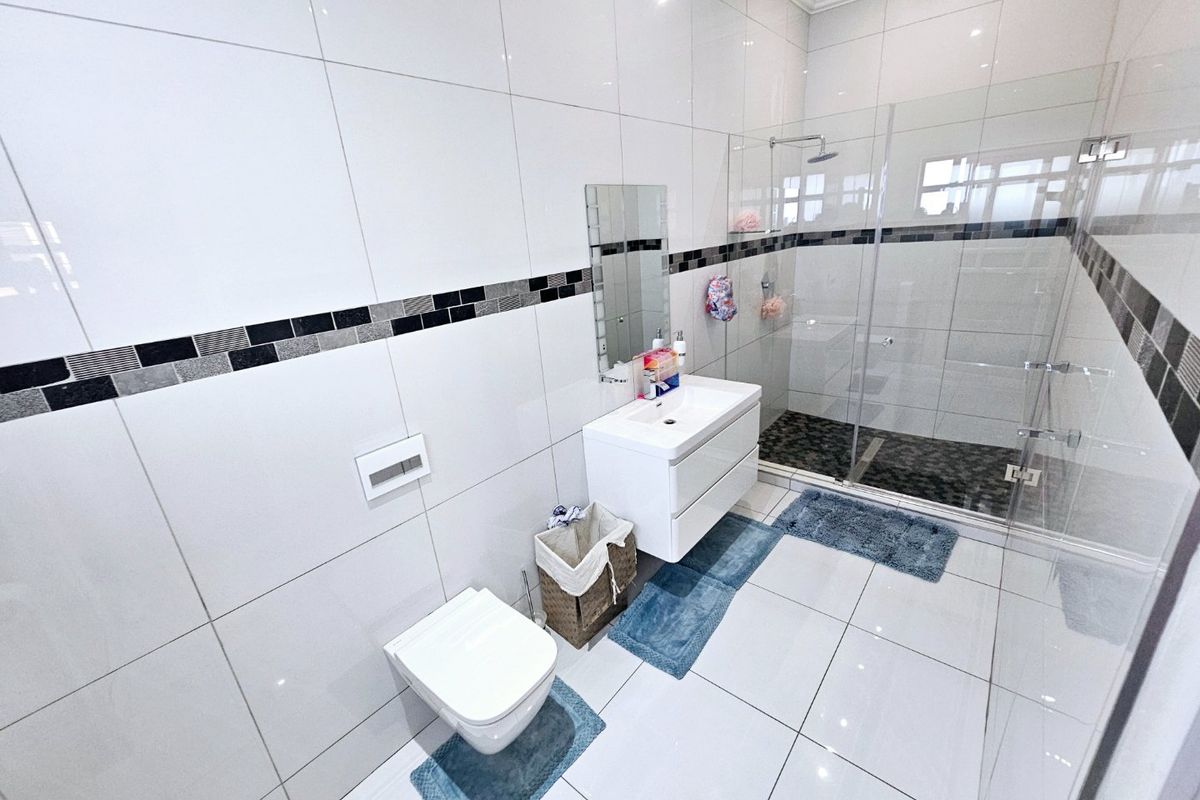 Modern bathroom featuring a wall-mounted vanity, wall-hung toilet, and a spacious walk-in shower with a glass screen and rain shower head.