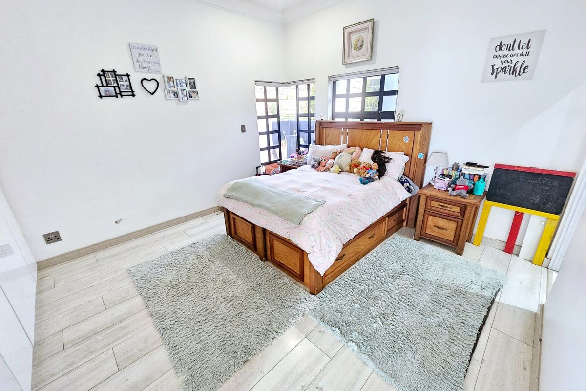 A bright bedroom featuring light-toned laminate flooring, coved ceilings, and corner windows that provide natural light.