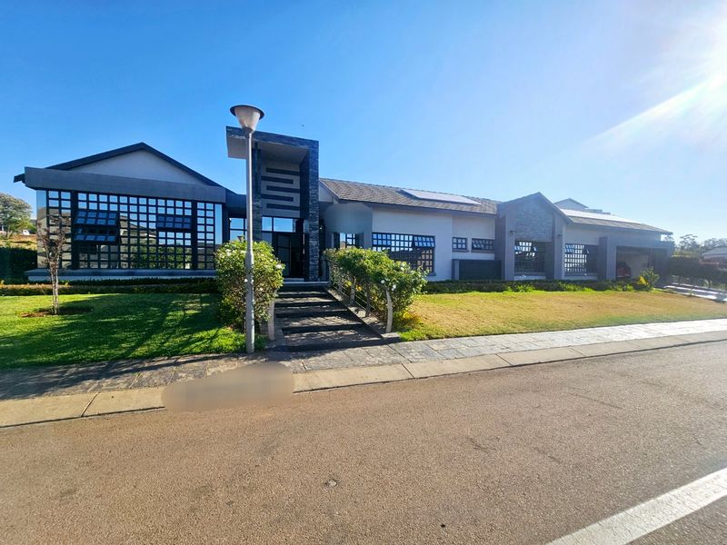 Modern single-story residence featuring stone cladding, large steel-framed windows, a paved entrance walkway, and integrated solar panels on a tiled roof.