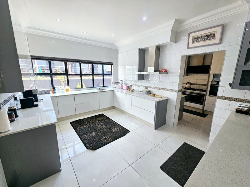 Modern kitchen featuring high-gloss cabinetry, stone countertops, tiled finishes, and an integrated scullery area, offering a clean and functional culinary space.