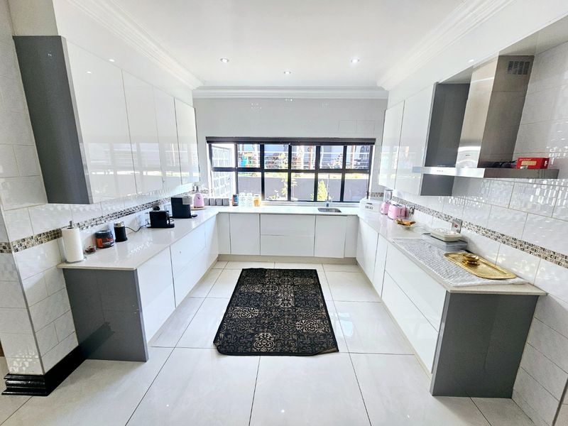 Modern kitchen featuring high-gloss white cabinetry, stone countertops, stainless steel extractor fan, and large format floor tiles with ample natural light.