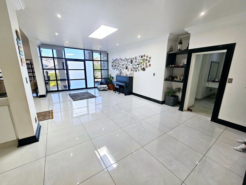 Spacious living area featuring large format porcelain floor tiles, a central skylight, recessed lighting, and expansive glass windows providing ample natural light.