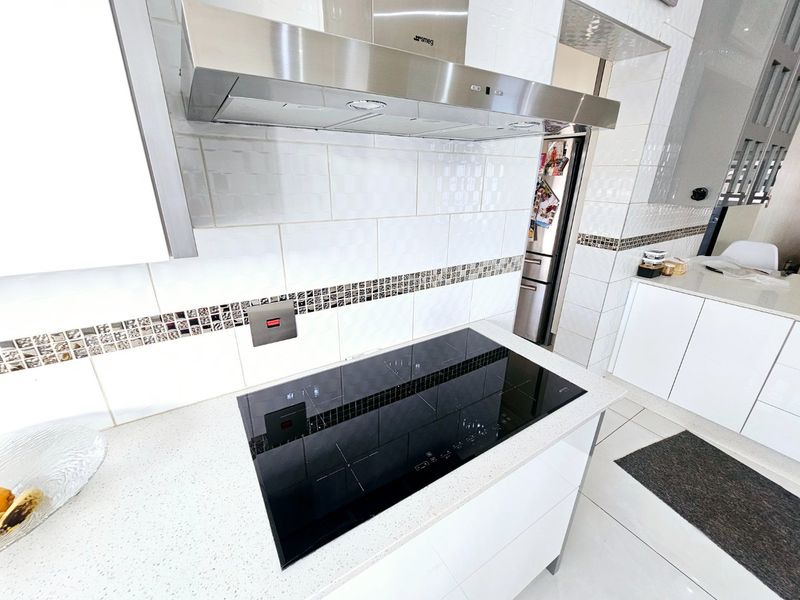 Modern kitchen featuring a sleek induction cooktop, stainless steel extractor fan, and clean white cabinetry with quartz countertops and a decorative tiled backsplash.