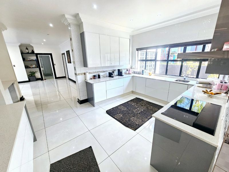 Modern kitchen featuring glossy white cabinetry, stone countertops, integrated induction hob, and large porcelain floor tiles with an open-plan layout.