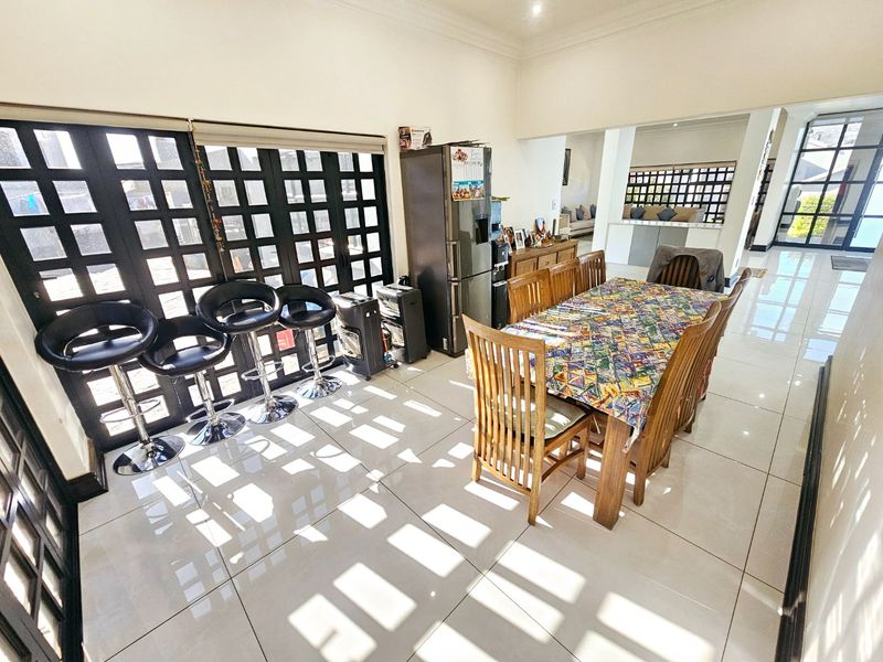 Spacious open-plan dining area featuring large grid-pattern glass doors, polished tiled flooring, and recessed ceiling lighting, creating a bright and airy living space.