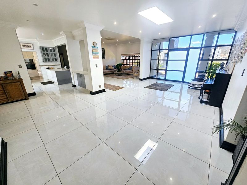 Spacious open-plan living area featuring polished porcelain tiles, a large skylight, and expansive glass windows, seamlessly connecting to a modern kitchen.