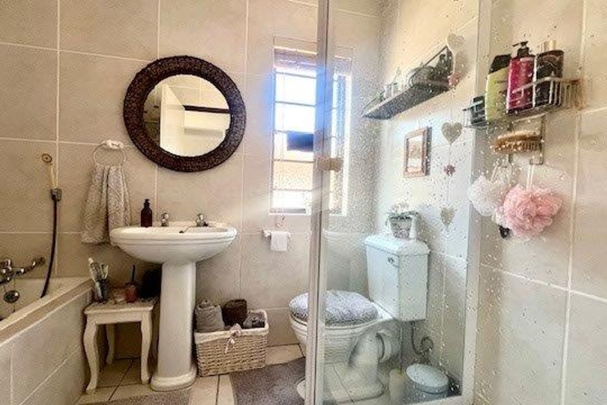 A functional bathroom featuring a pedestal basin, a bathtub with shower attachment, and a separate glass-enclosed shower cubicle with neutral wall tiling.