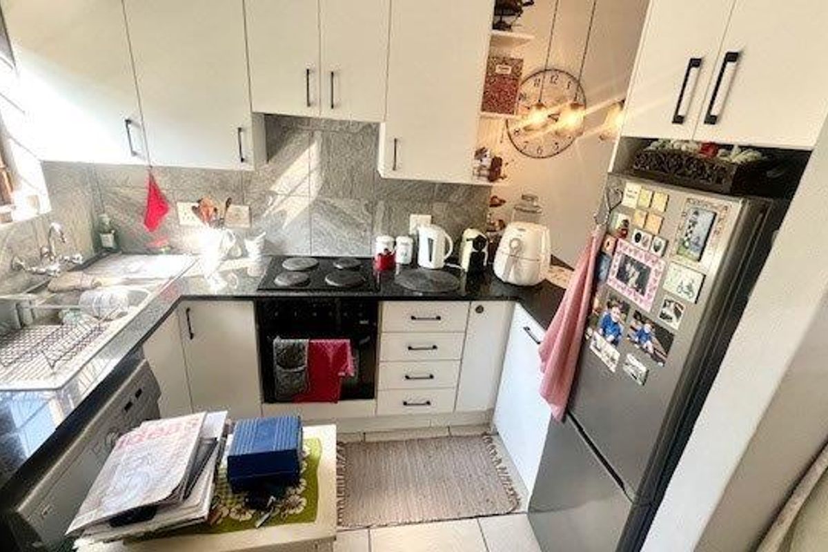 Compact kitchen featuring white cabinetry, dark countertops, a built-in electric hob and oven, and tiled splashbacks.