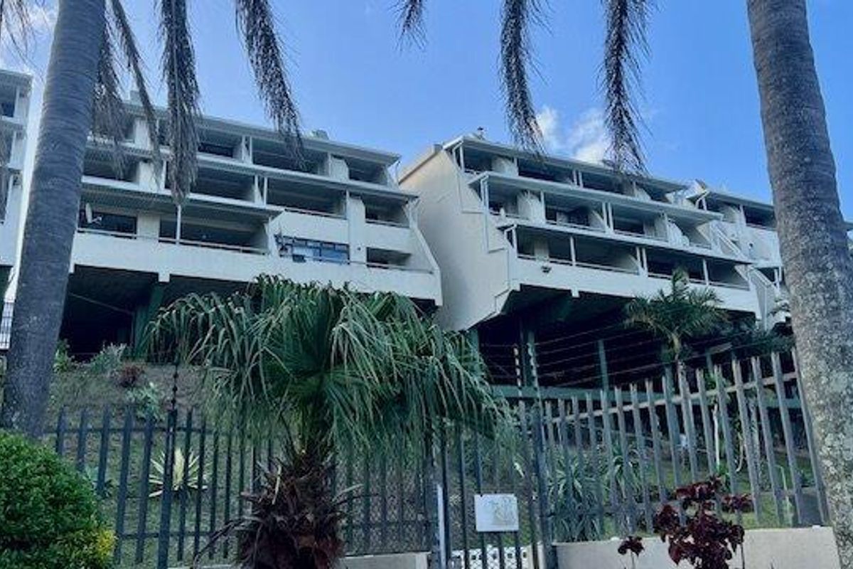 Rear elevation view of a multi-story apartment complex featuring tiered balconies and secure perimeter fencing.