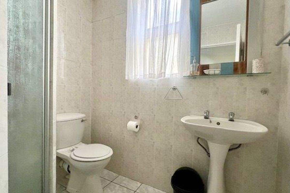 A functional bathroom featuring a pedestal washbasin, toilet, and a glass-enclosed shower, finished with neutral wall and floor tiling.
