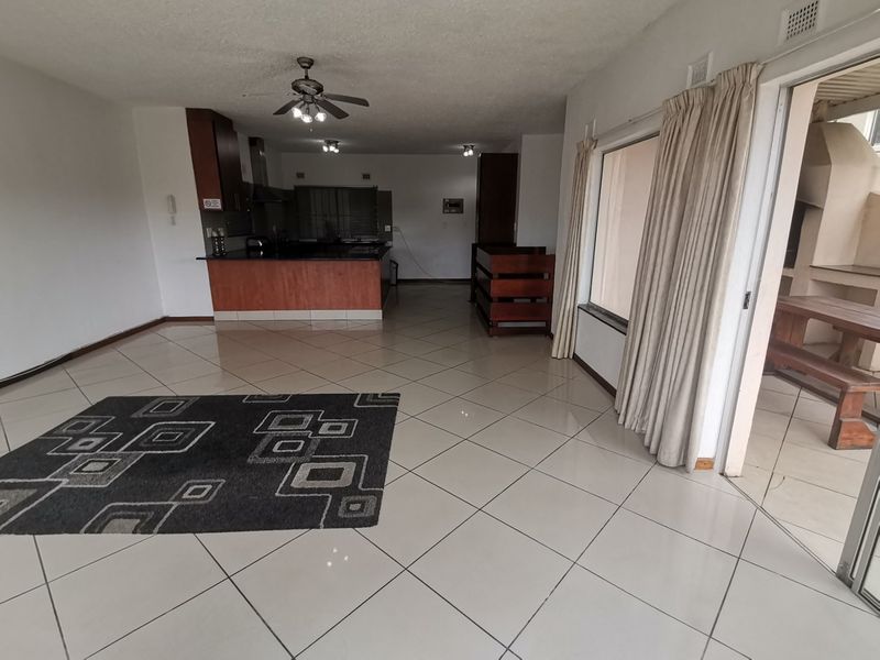 Open-plan living and kitchen area featuring tiled flooring, ceiling fan, and direct access to an outdoor patio through sliding glass doors.