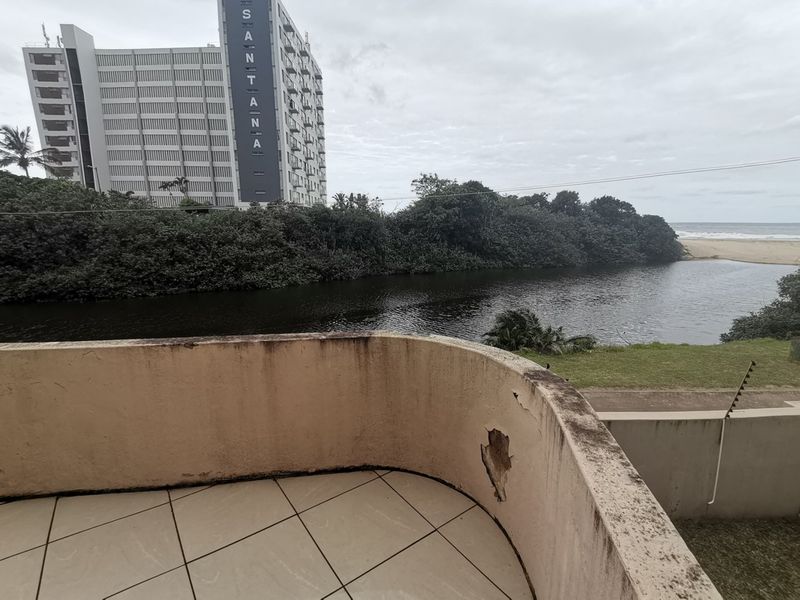 A balcony overlooking a river and coastal landscape, featuring tiled flooring and a concrete balustrade showing signs of significant weathering and structural surface damage.