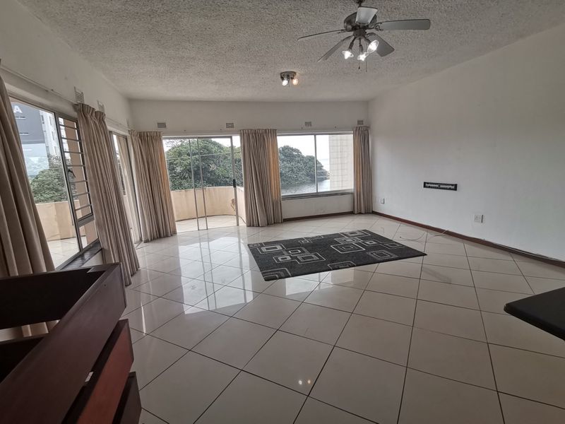 Spacious living area featuring large sliding glass doors, tiled flooring, and a ceiling fan, offering access to an outdoor balcony.