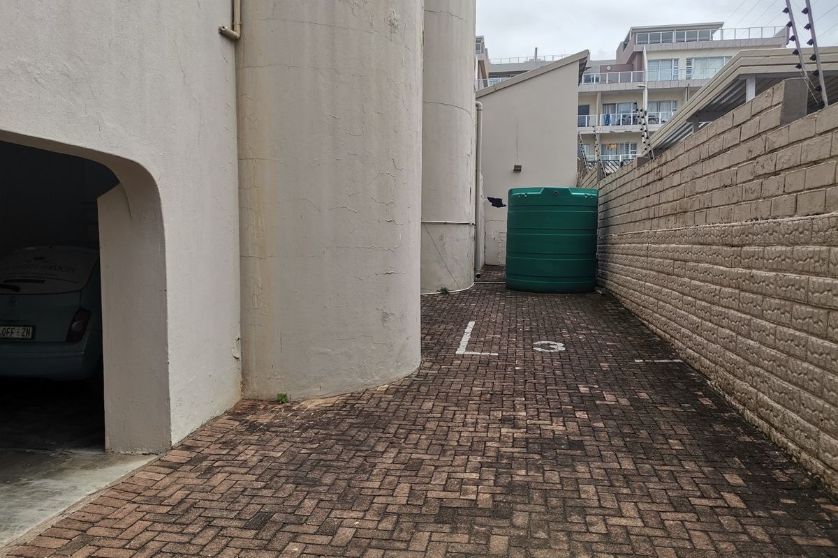 Rear exterior area featuring paved driveway, water storage tank, and boundary wall with electric fencing.