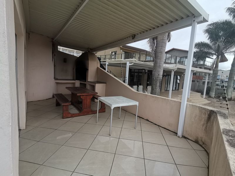 Covered patio area featuring a built-in braai, tiled flooring, and a low masonry wall, offering an outdoor entertainment space.