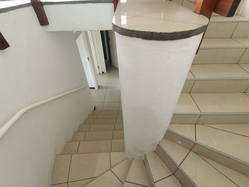 A view looking down a tiled staircase featuring a curved structural pillar and a wall-mounted handrail.