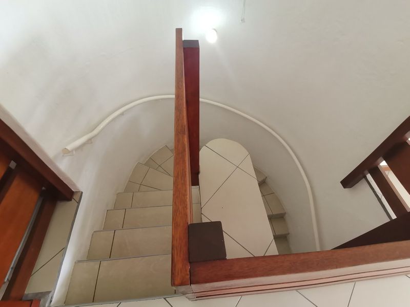 A view looking down a curved staircase featuring tiled steps and a wooden handrail, providing access between levels in the townhouse.