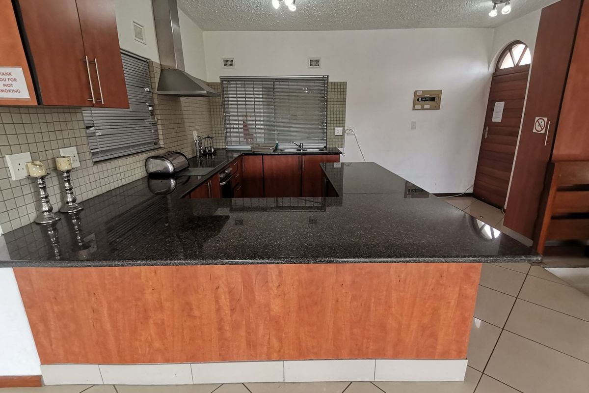 A functional kitchen featuring dark granite countertops, wood-finish cabinetry, a stainless steel extractor fan, and tiled flooring, offering a practical layout for daily use.