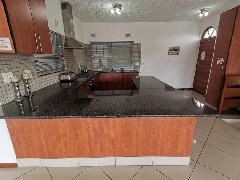A functional kitchen featuring dark granite countertops, wood-finish cabinetry, a stainless steel extractor fan, and tiled flooring, offering a practical layout for daily use.