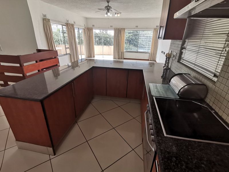 Open plan kitchen with granite countertops and electric hob, flowing into a living area with large windows and sliding doors leading to the exterior.