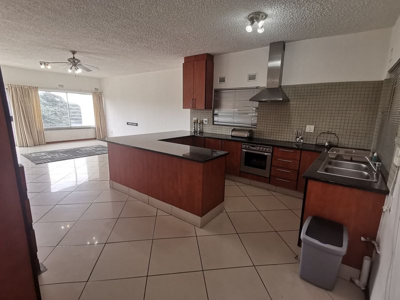 Open-plan kitchen and living area featuring dark wood cabinetry, granite countertops, stainless steel appliances, and neutral tiled flooring throughout.
