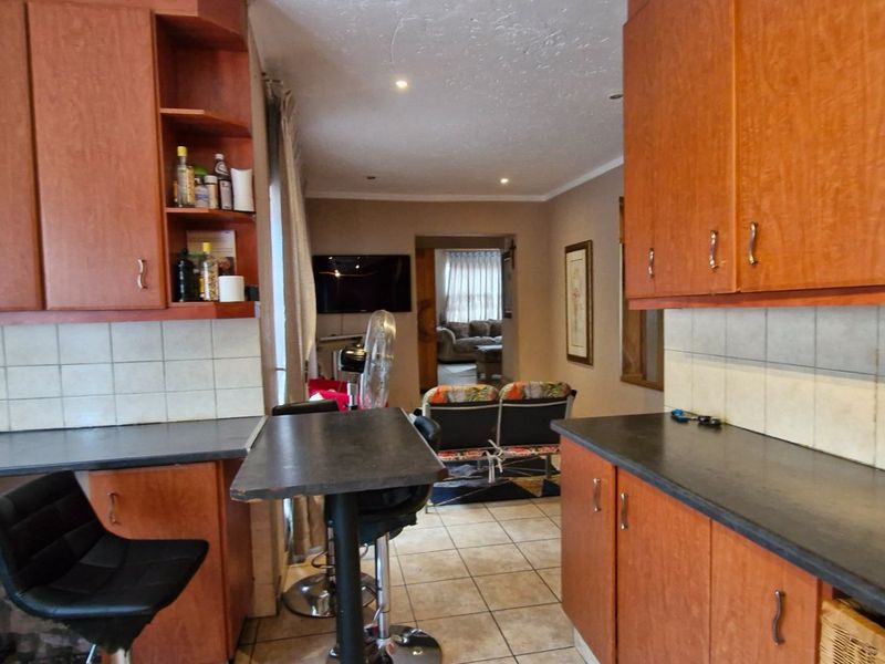 A functional kitchen featuring wood-look cabinetry, tiled backsplash, and dark laminate countertops, with an open-plan layout leading into the living area.