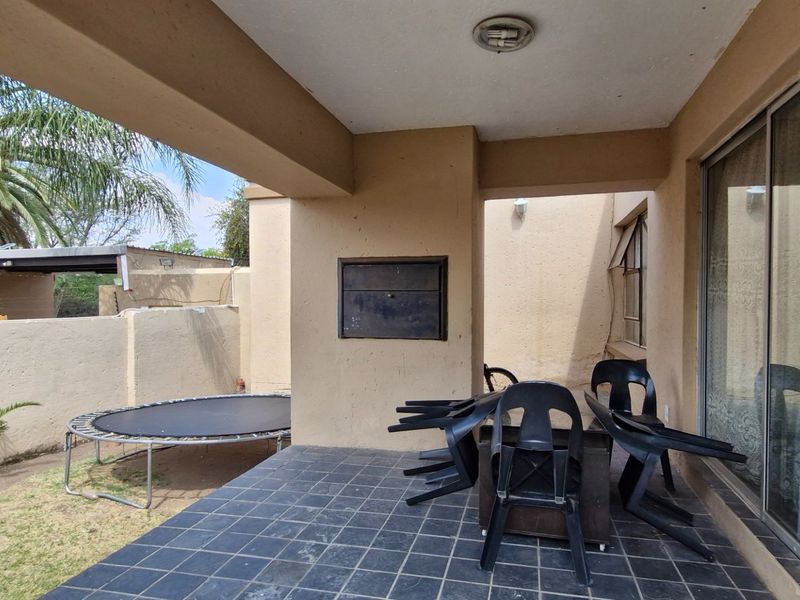 A covered patio area featuring tiled flooring and a built-in braai, providing direct access to the garden through large sliding glass doors.