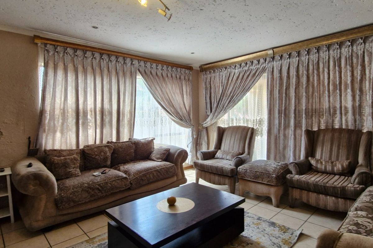 A living room featuring tiled flooring and large windows with curtain rails, showing signs of wear on the wall surfaces.