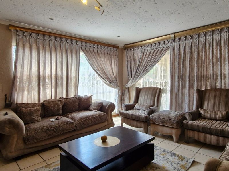 A living room featuring tiled flooring and large windows with curtain rails, showing signs of wear on the wall surfaces.