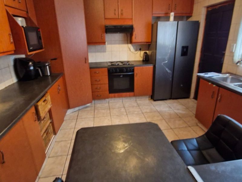 A functional kitchen featuring wood-tone cabinetry, dark countertops, built-in oven with gas hob, and tiled flooring with integrated laundry plumbing.
