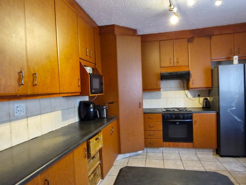 A functional kitchen featuring extensive wooden cabinetry, laminate countertops, built-in oven, and hob with a tiled backsplash and flooring.