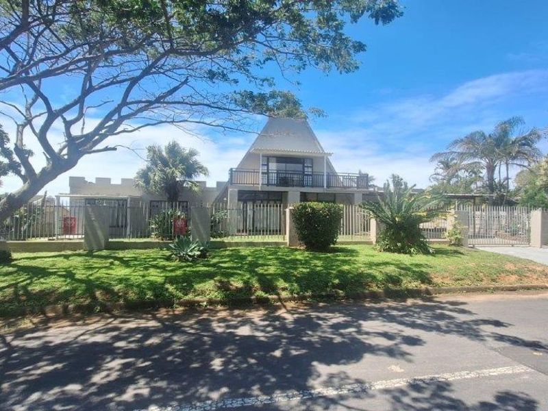 Front view of a residential property featuring a unique pitched roof design, balcony, and secure metal perimeter fencing with a paved driveway.