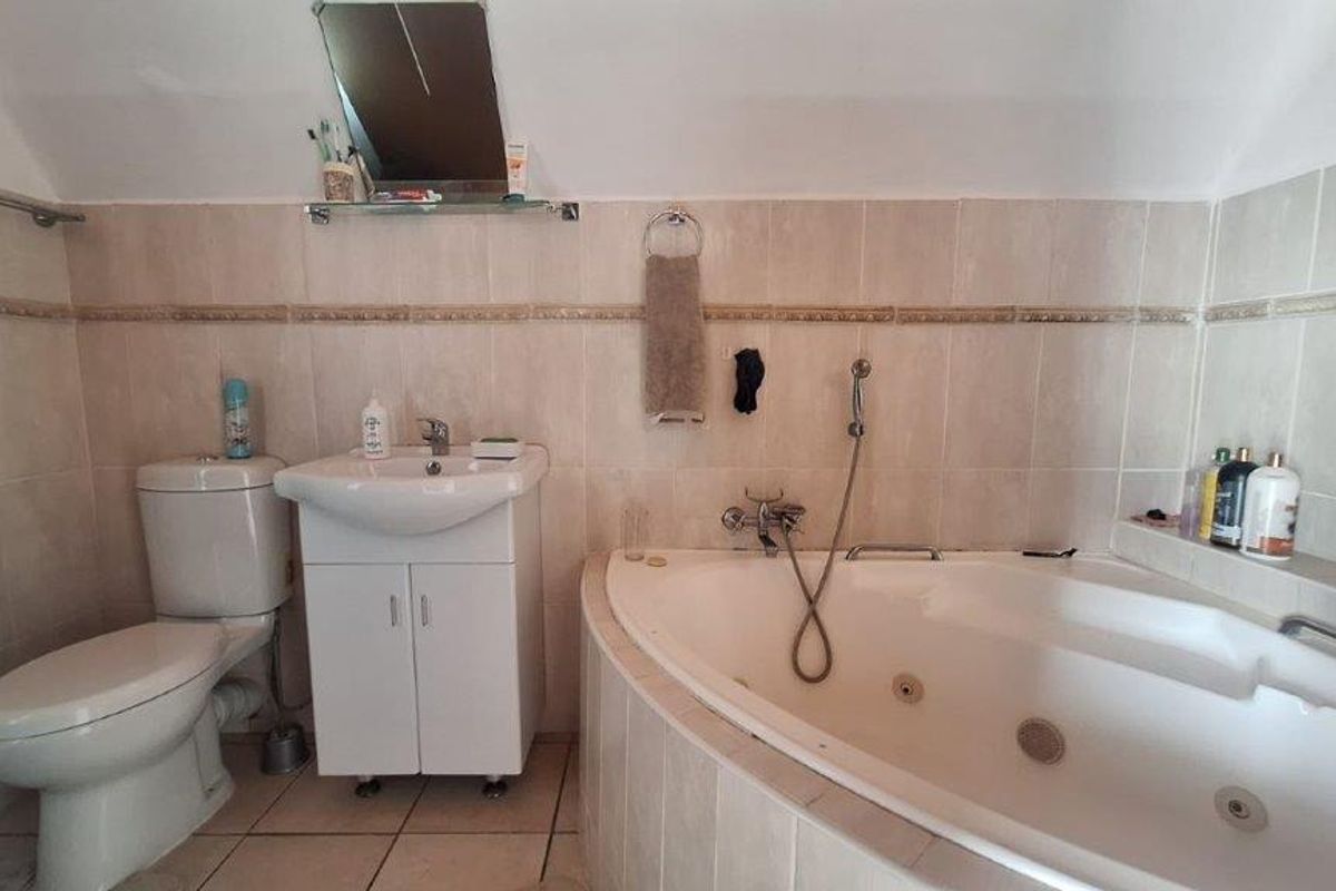 A functional bathroom featuring a corner bathtub with shower mixer, a vanity unit with washbasin, and a toilet, finished with neutral wall and floor tiles.