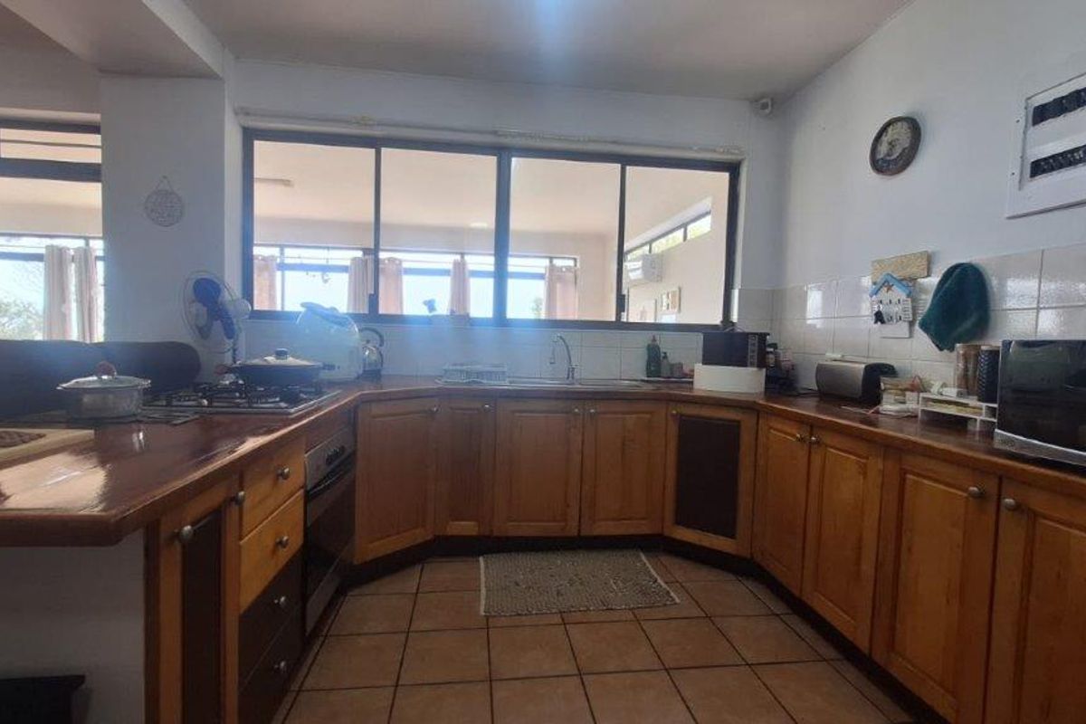 A functional kitchen featuring wooden cabinetry, tiled splashbacks, gas hob, built-in oven, and tiled flooring with ample natural light from large sliding windows.