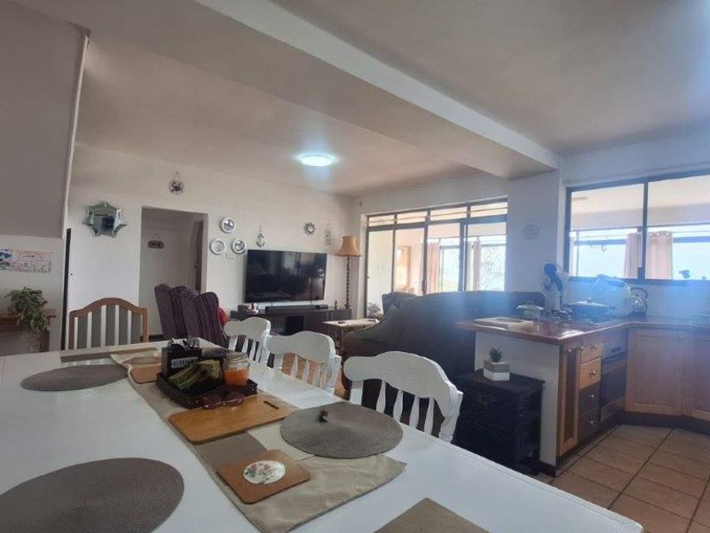 Open-plan living and dining area featuring a functional kitchen with built-in cabinetry, tiled flooring, and large windows providing natural light.