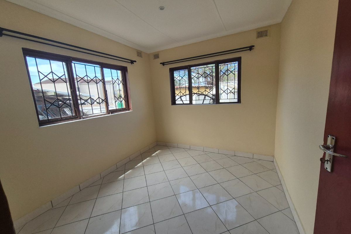 A bright, empty bedroom featuring neutral walls, tiled flooring, and windows fitted with security bars.