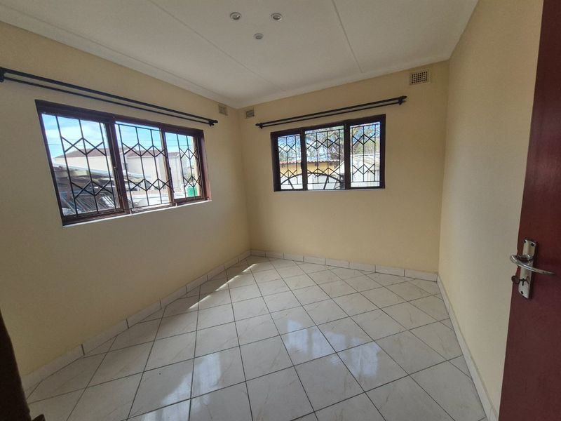 A bright, empty bedroom featuring neutral walls, tiled flooring, and windows fitted with security bars.