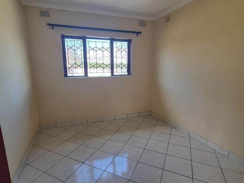 A clean, empty bedroom featuring neutral walls, tiled flooring, and security bars on the window, providing a blank canvas for personalization.