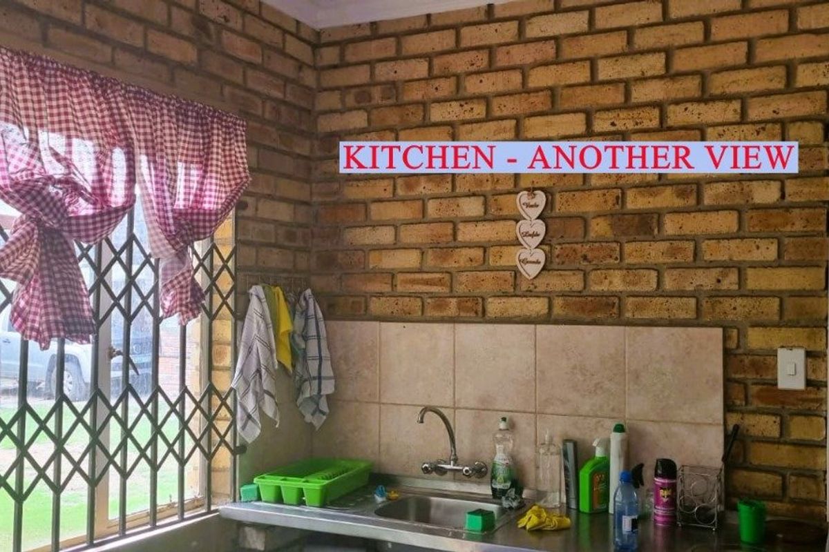 A rustic kitchen area featuring exposed face-brick walls, a stainless steel sink, and security gate window protection.