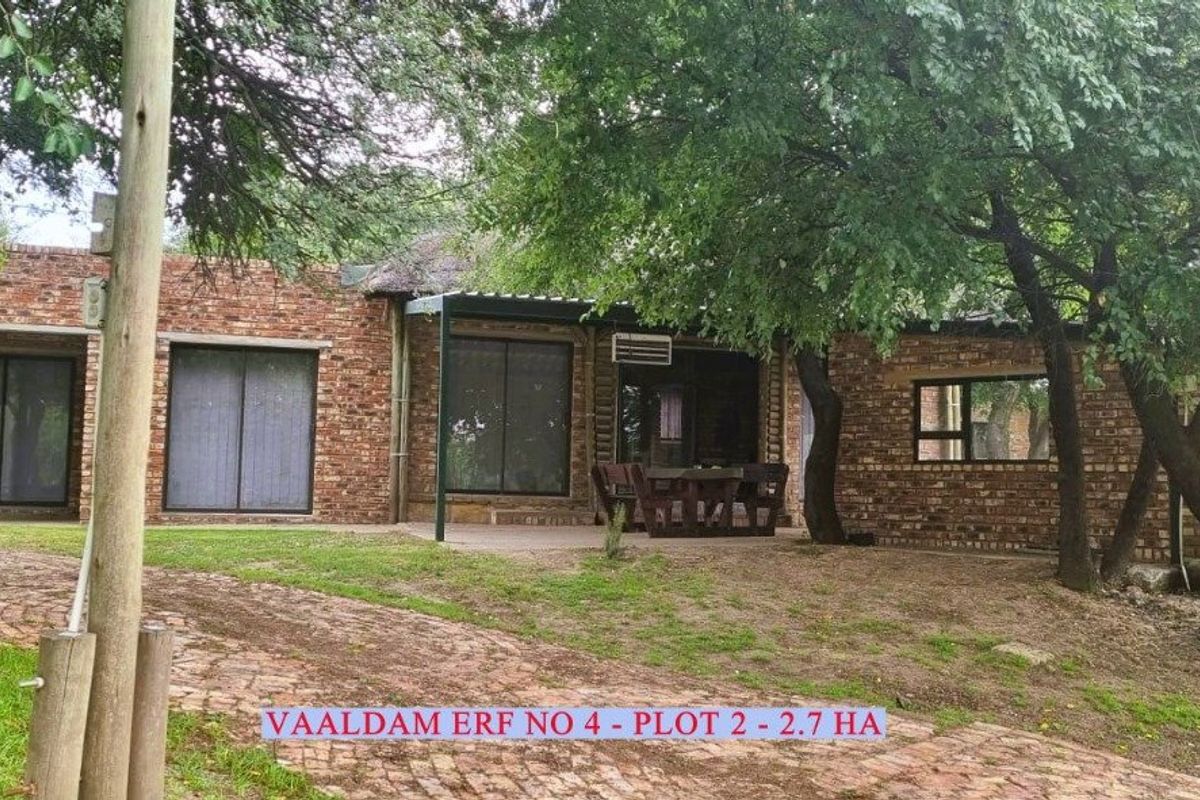 A rustic face-brick farmhouse exterior featuring a covered patio area, mature trees, and a brick-paved driveway on a spacious 2.7-hectare plot.