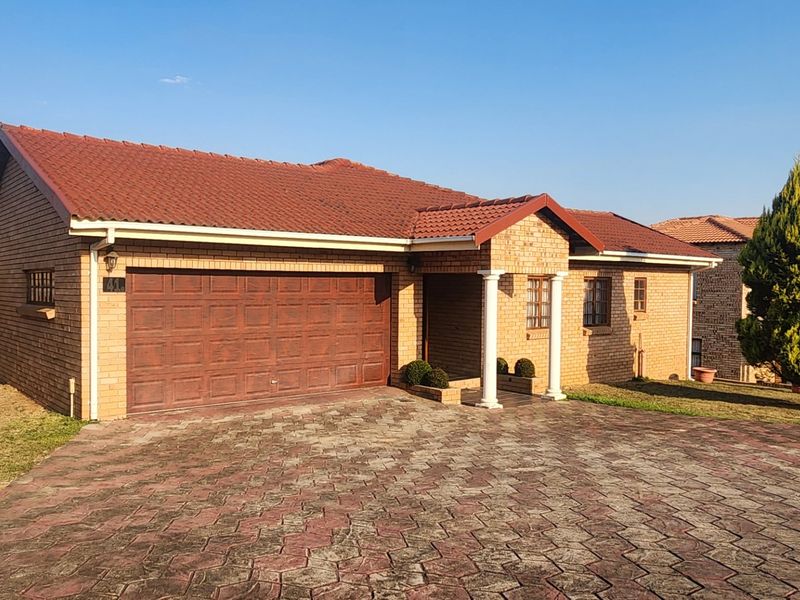 A well-maintained single-story brick house featuring a tiled roof, a double garage, and a paved driveway with a covered entrance porch.