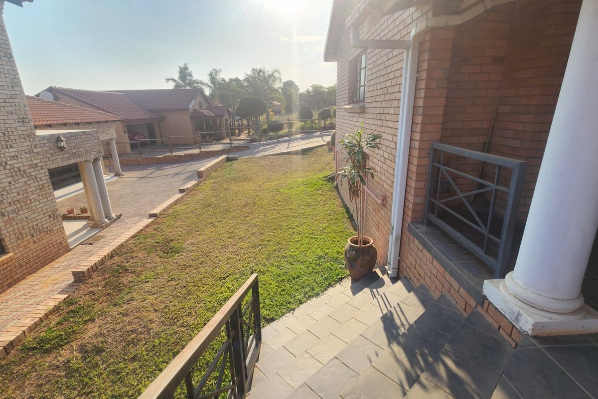 A view of the rear exterior featuring a brick facade, a tiled patio area with metal railings, and a paved driveway leading to the property.