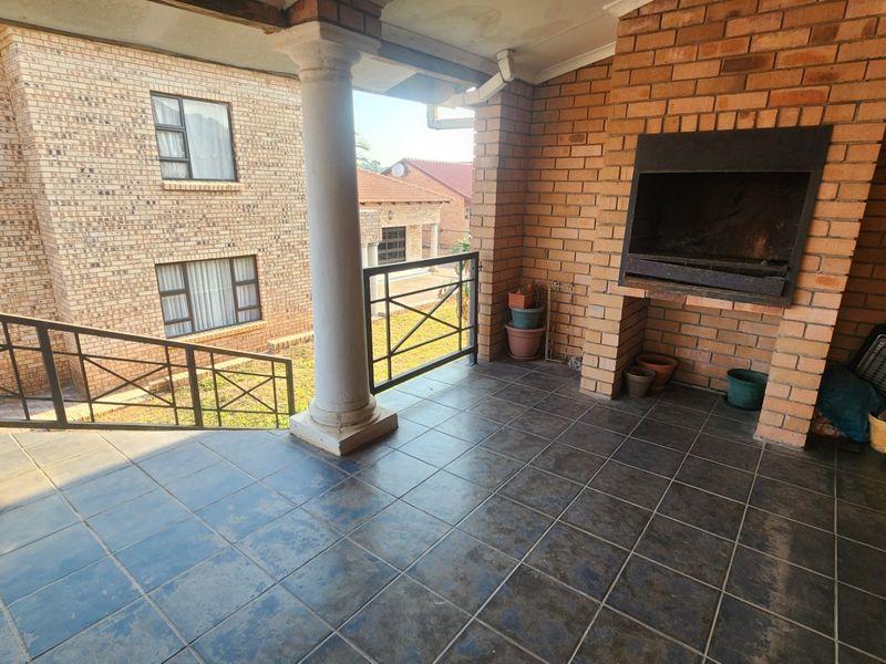 Covered patio area featuring a built-in brick braai, tiled flooring, and a structural column, overlooking the surrounding property grounds.