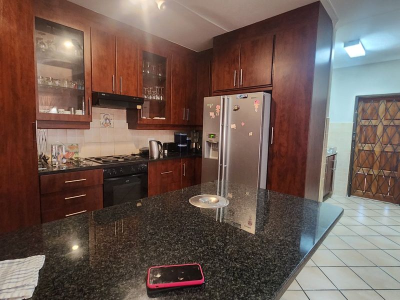 A functional kitchen featuring dark wood cabinetry, granite countertops, a central island, and tiled flooring, leading to a secondary area with a security gate.