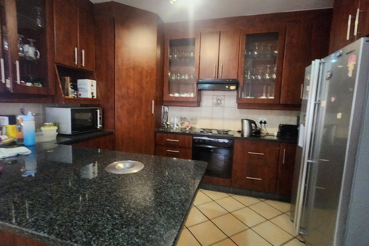 A functional kitchen featuring dark wood cabinetry, granite countertops, tiled flooring, and integrated appliances including an oven and extractor fan.