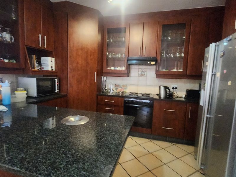 A functional kitchen featuring dark wood cabinetry, granite countertops, tiled flooring, and integrated appliances including an oven and extractor fan.