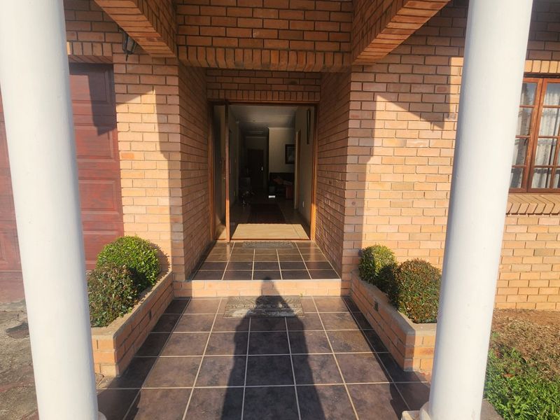 Front entrance of a brick house featuring a tiled porch, concrete columns, and built-in brick planters leading to the main doorway.