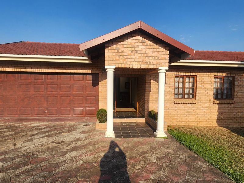 Front elevation of a single-story brick house featuring a double garage, covered entrance porch with decorative columns, and a paved driveway.