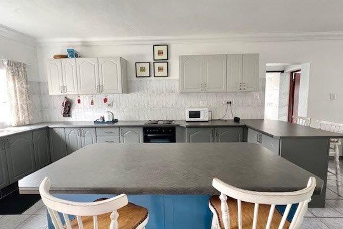 Spacious kitchen featuring grey built-in cabinetry, a central island with seating, tiled backsplash, and integrated cooking appliances.