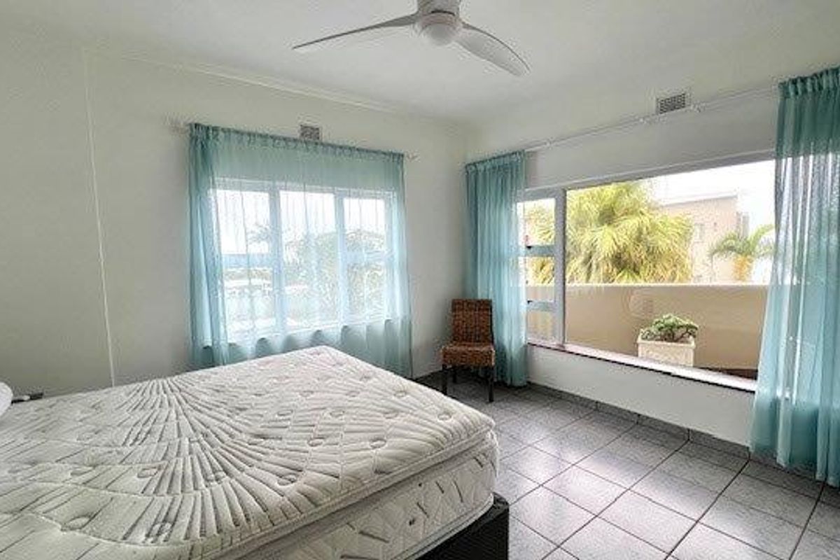 A bright bedroom featuring tiled flooring, a ceiling fan, and large windows with direct access to an outdoor balcony area.